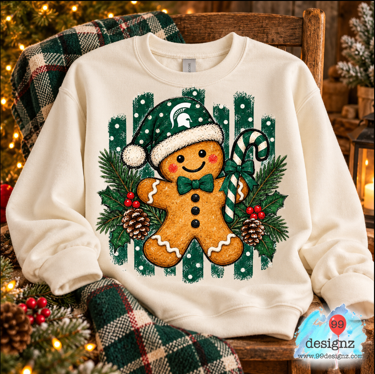 Cream sweatshirt mockup showing a Michigan State gingerbread character in a green Spartan Santa hat with candy cane and greenery; PNG artwork only.